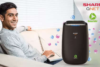 A happy Indian man working with his laptop on the sofa with SHARP QNET SmartAir in the frame