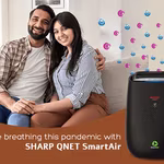 A young couple sitting on the couch with SHARP QNET SmartAir air purifier in the frame