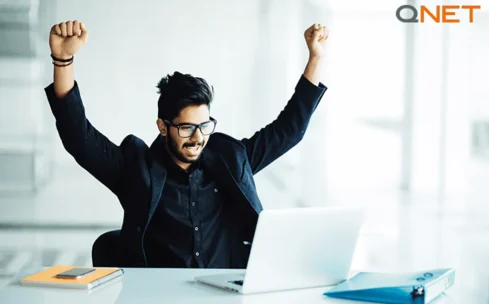 young indian business man in a suit celebrating in front of his laptop