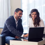 man and woman sitting at computer smiling working